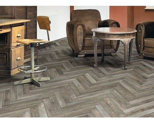 Raumszene mit Fischgrät-Designboden, Stühlen, Sessel und Tisch.