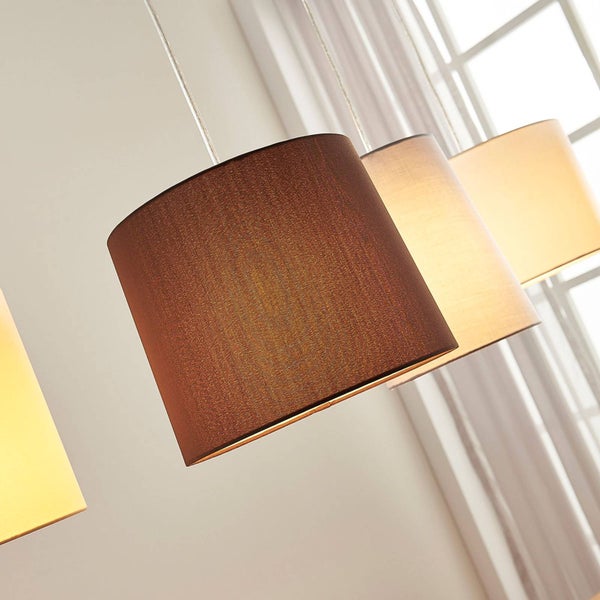 Pendelleuchte mit Stoffschirmen in verschiedenen Brauntönen, in einer Reihe hängend vor einem Fenster.