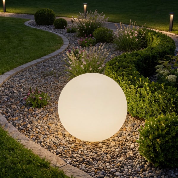 Leuchtende Gartenkugel in einem Beet mit Kieselsteinen und verschiedenen Pflanzen bei Nacht.