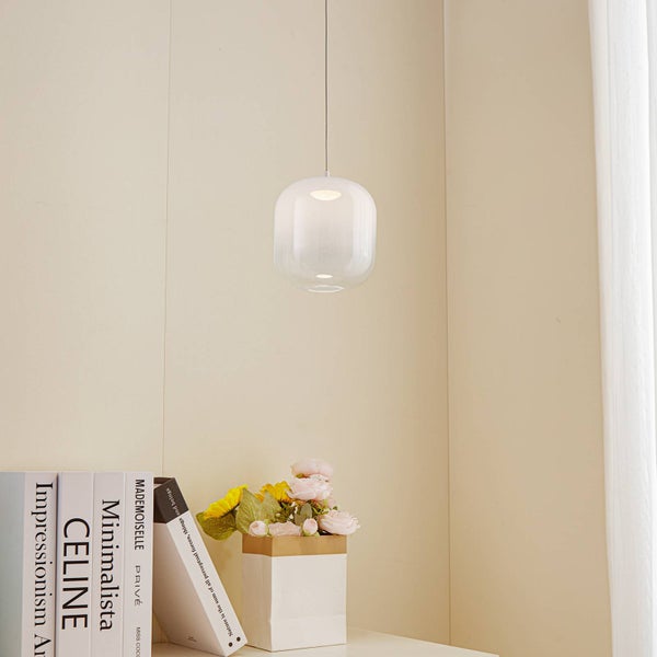 Moderne Pendelleuchte aus Glas über einem Tisch mit Büchern und Blumen in einem hellen, minimalistischen Raum.