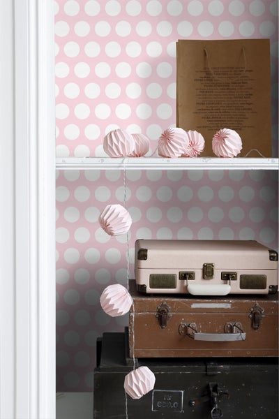 Regal mit Dekoration, bestehend aus Papiergirlande, Papiertüten und Vintage-Koffern vor gepunkteter Tapete.