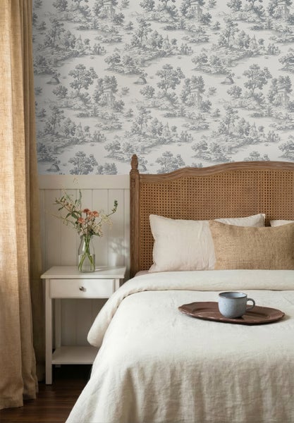 Vliestapete mit grauem Toile-de-Jouy-Muster in einem hellen Schlafzimmer mit Rattanbett, weißem Nachttisch und Holzpaneelen.