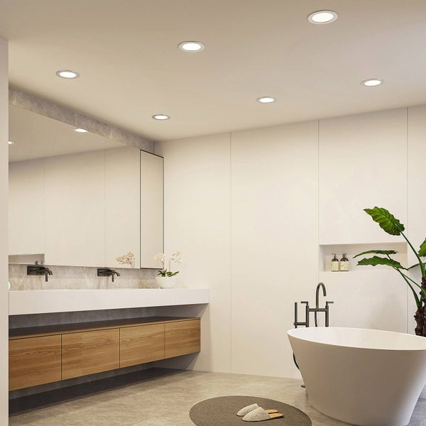 Modernes Badezimmer mit runden LED-Einbaustrahlern an der Decke, einer freistehenden Badewanne und einem Waschtisch mit Unterschrank in Holzoptik.