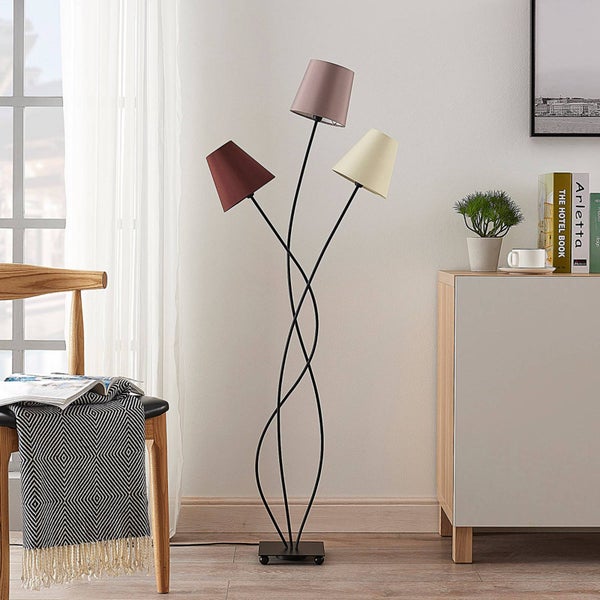 Dreiflammige Stehleuchte mit schwarzen Metallstäben und Stoffschirmen in einem hellen, modernen Wohnzimmer neben einer Kommode.