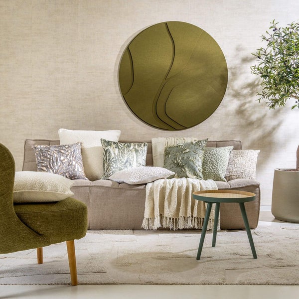 Wohnzimmer mit Sofa, Kissen, Sessel, Beistelltisch, Zimmerpflanze und Wanddekoration für eine gemütliche Atmosphäre.