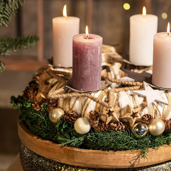 Dekorativer Adventskranz mit vier brennenden Stumpenkerzen, geschmückt mit Tannengrün, Zapfen, Sternen und Kugeln in einer Holzschale.