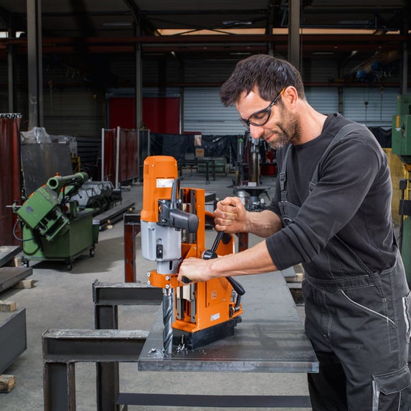 Ein Handwerker bedient eine Magnetkernbohrmaschine in einer Werkstatt, um ein Loch in eine dicke Metallplatte zu bohren.