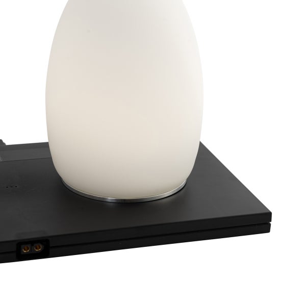 Tischleuchte mit weißem ovalem Schirm auf einer schwarzen flachen Ladestation.