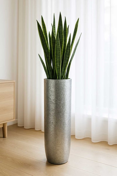 Hohe silberne Bodenvase mit strukturierter Oberfläche und Sansevieria in einem hellen Wohnzimmer mit Holzfußboden.