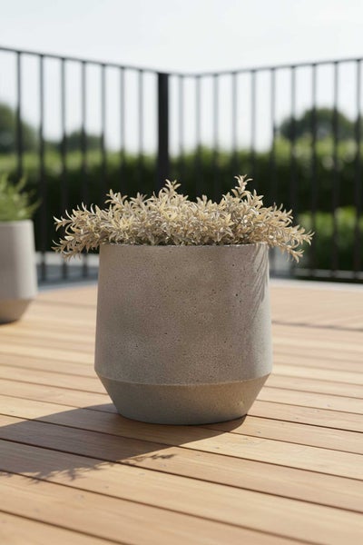 Runder Pflanzkübel in Betonoptik auf einer Holzterrasse, modernes Design mit einer kleinen Pflanze.