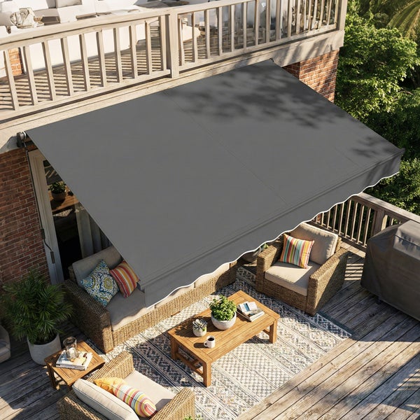 Graue Markise über einer hölzernen Terrasse mit Polyrattan-Gartenmöbeln, Holztisch und Teppich vor einer Ziegelwand.
