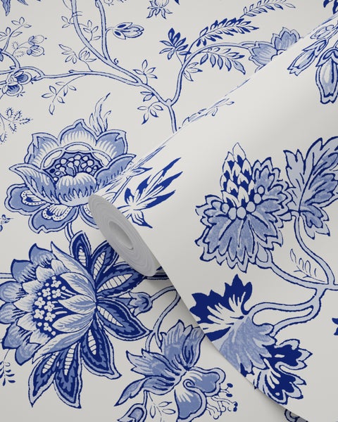 Vliestapete mit blauem floralem Muster aus blühenden Blumen und filigranen Zweigen. Eine Rolle ist teilweise ausgerollt.
