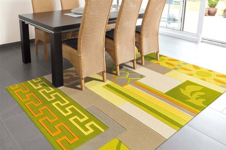 Moderner Wohnzimmerteppich mit geometrischem Muster und Blumenmotiven unter einem Esstisch mit Rattan-Stühlen auf einem Fliesenboden.