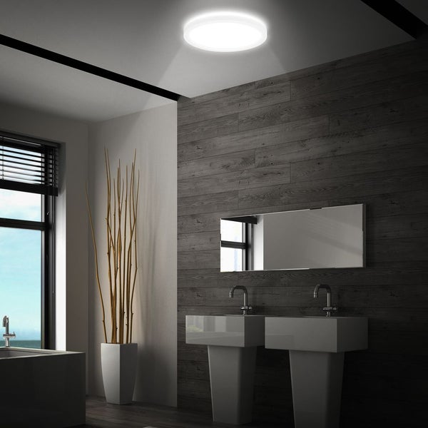 Moderne Badezimmer-Szene mit einer runden LED-Deckenleuchte über zwei weißen Waschtischen und einer Wand in dunkler Holzoptik.