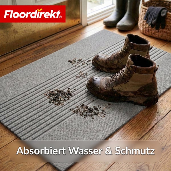 Floordirekt Logo. Gerippte Fußmatte auf einem Holzboden in einem Eingangsbereich mit schmutzigen Arbeitsschuhen. Absorbiert Wasser und Schmutz.