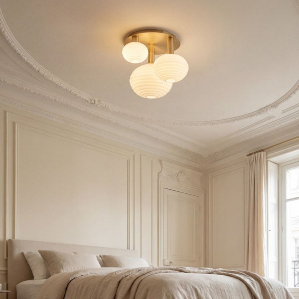 Klassisches helles Schlafzimmer mit Wandleisten und einer dreiflammigen Deckenleuchte mit geriffelten Glaskugeln und goldfarbenem Fuss.