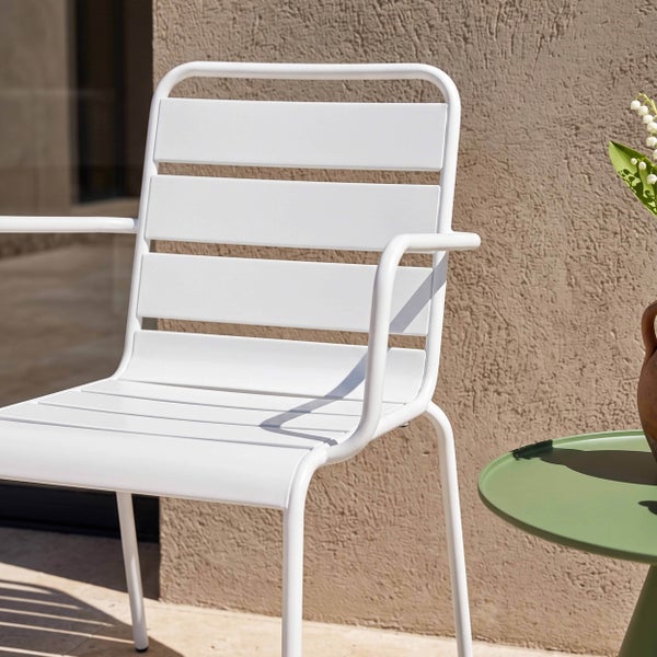 Weißer Gartenstuhl aus Metall mit Armlehnen und Latten-Design auf einer Terrasse vor einer Wand.