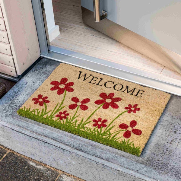 Fußmatte aus Kokosfaser mit Willkommensgruß und Blumenmotiv vor einer Haustür