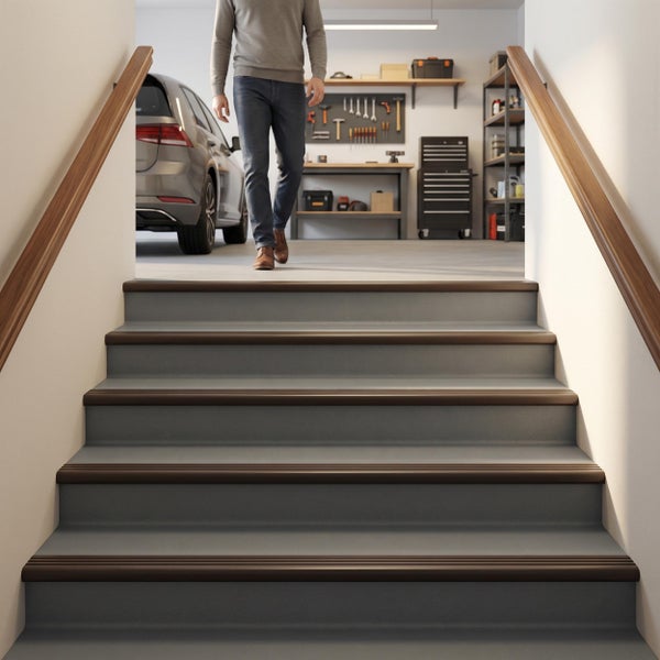 Treppe mit Holzhandläufen führt in eine organisierte Garage mit Werkbank, Werkzeugwand, Regalen und einem geparkten Auto im Hintergrund.