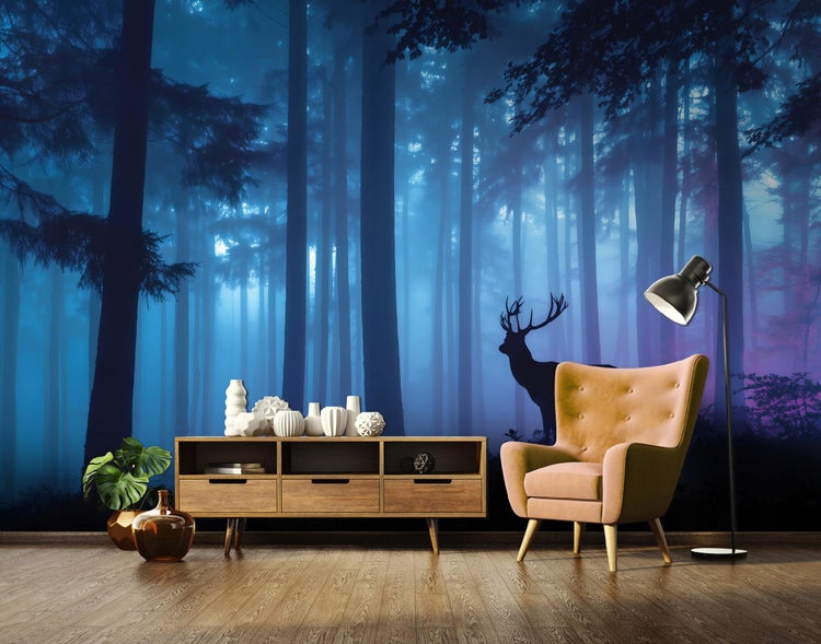 Fototapete mit Nebelwald, hohen Bäumen und Hirsch-Silhouette in Blau und Violett. Davor ein Sideboard aus Holz, ein Sessel und eine Stehleuchte.