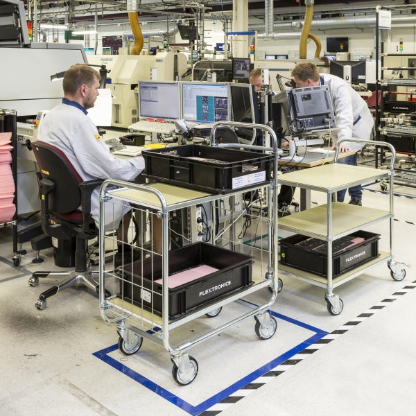 Szene einer Fabrikhalle mit Arbeitern an Computern und Rollwagen mit Behältern