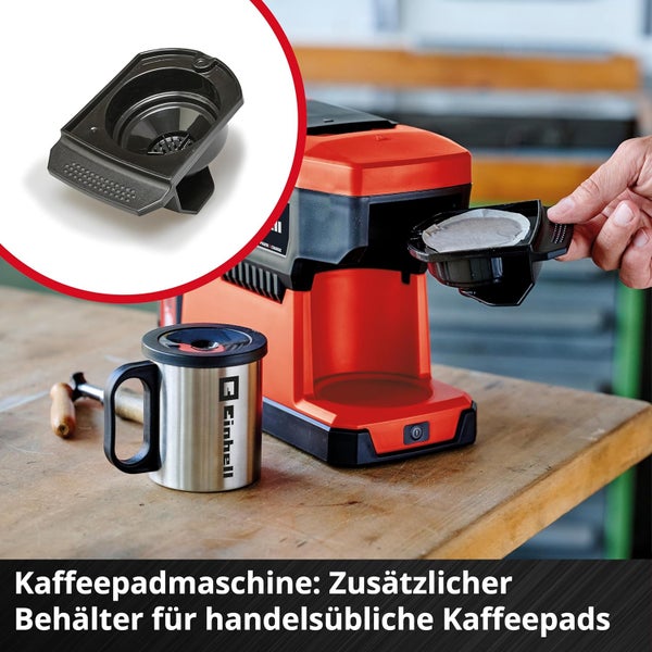 Einhell Akku-Kaffeepadmaschine auf einer Werkbank. Eine Hand setzt den zusätzlichen Behälter für Kaffeepads ein. Daneben steht ein Edelstahlbecher.