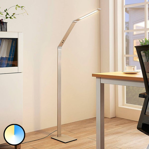 Moderne LED-Stehleuchte aus Metall mit verstellbarem Arm in einem hellen Arbeitszimmer neben einem Schreibtisch und Symbol für einstellbare Farbtemperatur.
