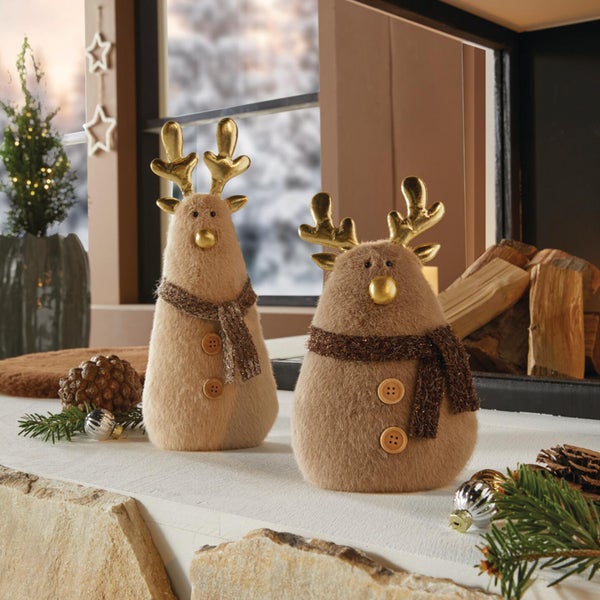 Zwei flauschige Weihnachtsrentier Figuren mit goldenem Geweih und Schal als weihnachtliche Tischdekoration auf einem Kaminsims.