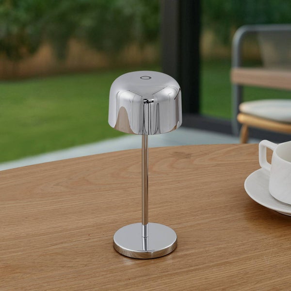 Moderne, pilzförmige Tischleuchte aus verchromtem Metall auf einem Holztisch in einer hellen Umgebung.