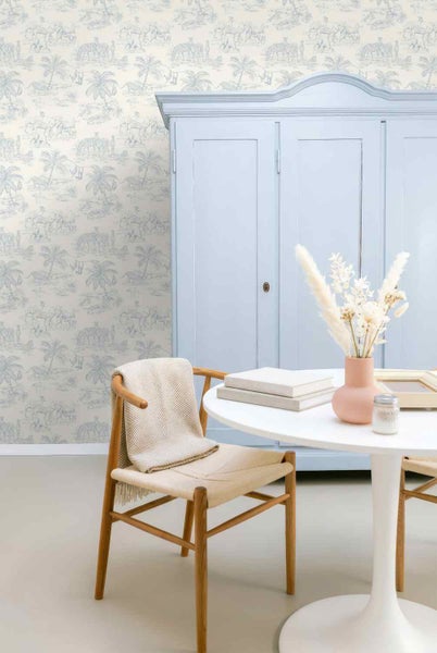 Vliestapete mit Safari-Motiv, Palmen und Zebras im Toile-de-Jouy-Stil in einem hellen Raum mit Schrank, Tisch und Stuhl.