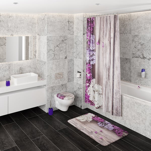 Modernes Badezimmer mit Fliesen in Steinoptik, Duschvorhang und Badematte mit Fliederblüten und Holzoptik sowie weißem Waschbecken und WC.