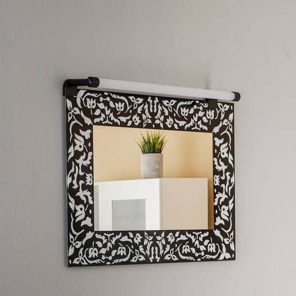 Rechteckiger Wandspiegel mit floralem Ornamentrahmen und einer darüber montierten LED Bilderleuchte.