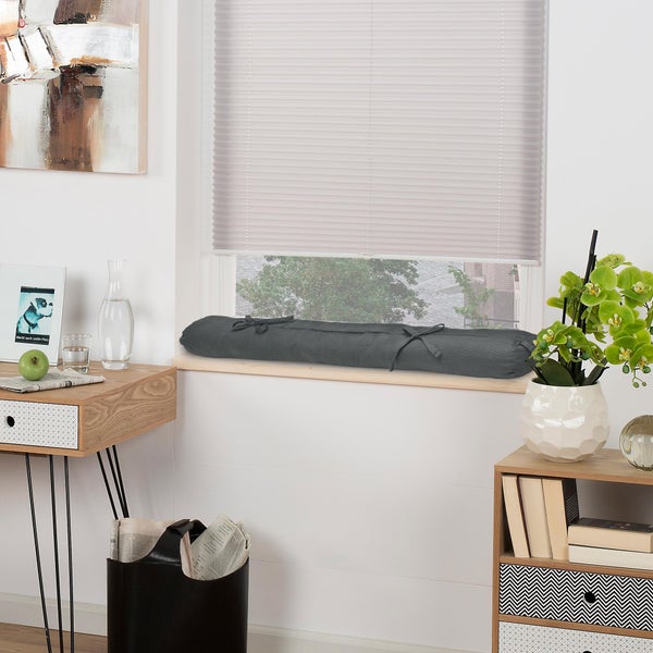 Dunkelgrauer Zugluftstopper aus Stoff auf einer hellen Fensterbank in einem hellen, modern eingerichteten Zimmer.