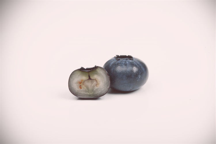 Eine ganze Blaubeere neben einer aufgeschnittenen Blaubeere.