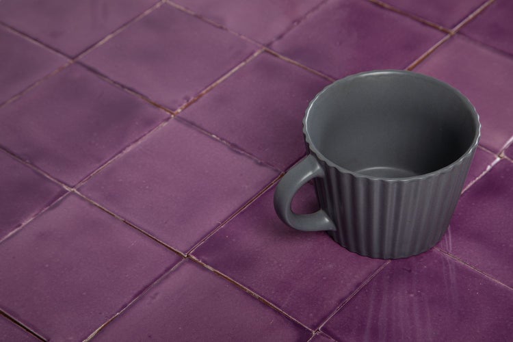 Nahaufnahme von quadratischen, violetten Fliesen mit einer grauen Tasse.