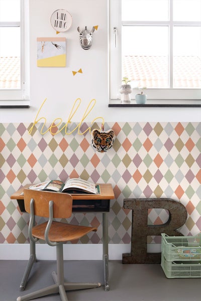 Helles Kinderzimmer mit Rautenmuster-Tapete, einem hölzernen Schultisch, einem Metall-Buchstaben B und Wanddekorationen mit Tiermotiven.