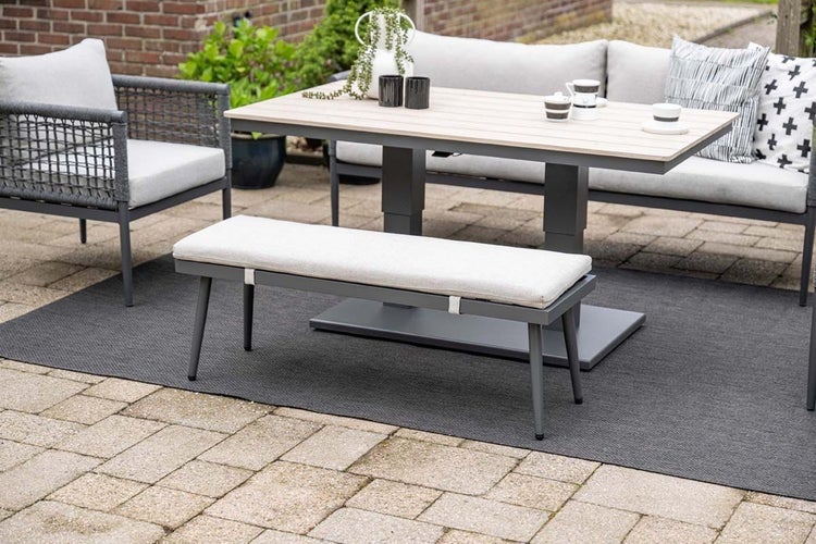 Moderne Gartenlounge-Sitzgruppe mit Sofa, Sessel, Sitzbank und höhenverstellbarem Tisch auf einer gepflasterten Terrasse mit Teppich.