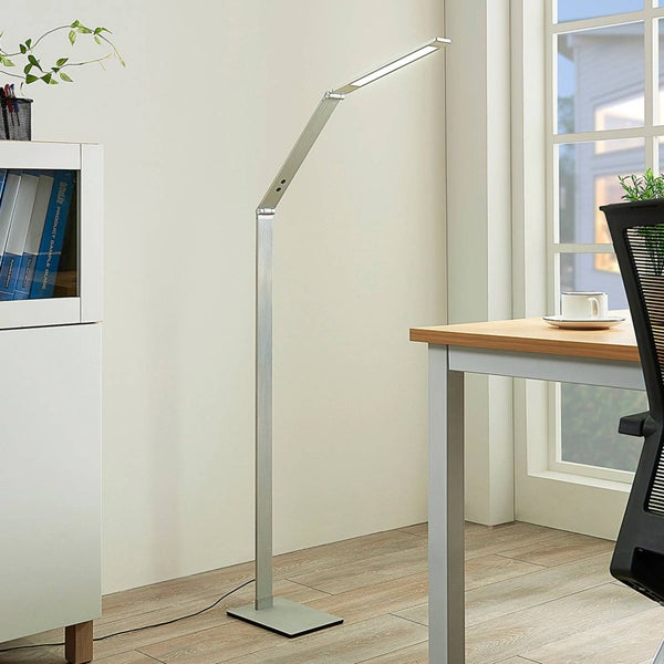 Moderne LED-Stehleuchte in Silber mit verstellbarem Arm, platziert in einem hellen Arbeitszimmer neben einem Schreibtisch.