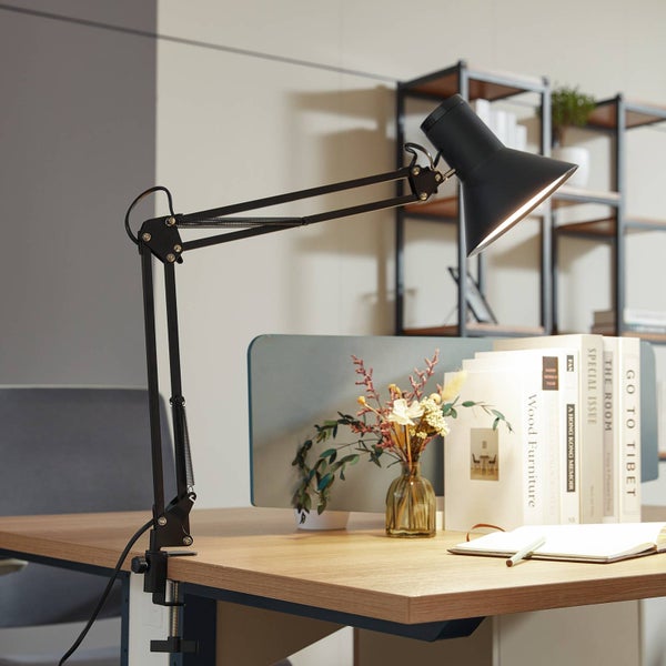Schwarze Schreibtischleuchte aus Metall mit verstellbarem Gelenkarm und Klemmfuß auf einem Holzschreibtisch mit Büchern und einer Blumenvase.