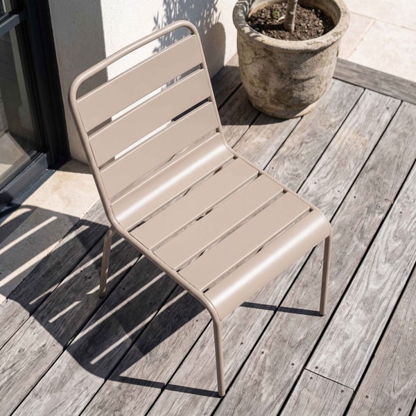 Moderner Gartenstuhl aus Metalllatten auf einer Holzterrasse neben einem Pflanzgefäß.
