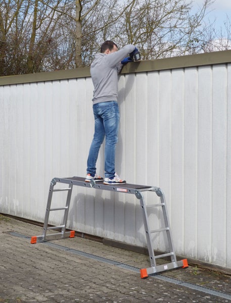 Ein Mann arbeitet auf einer Aluminium-Arbeitsbühne mit einer Bohrmaschine an einer Wand.
