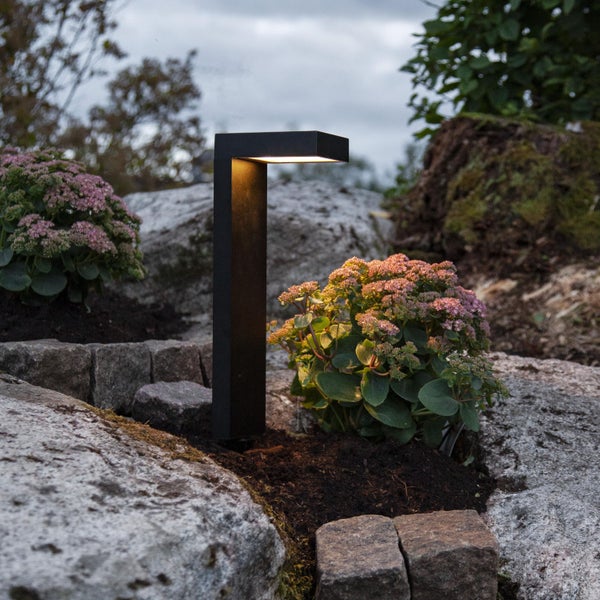 Eine Gartenleuchte zwischen Steinen und Pflanzen in einem Garten.
