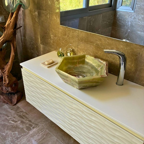 Modernes Badezimmer mit hexagonalem Aufsatzwaschbecken aus Onyx auf einem weißen Unterschrank mit Wellenstruktur und einer verchromten Armatur.