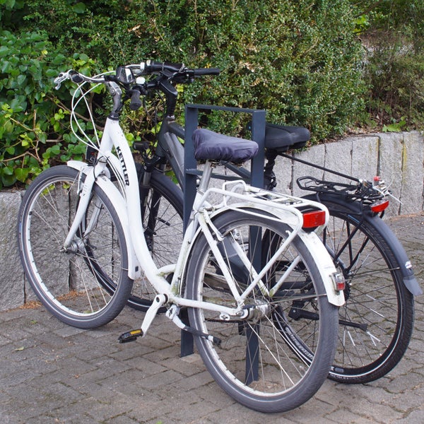 Zwei Fahrräder, ein weißes Kettler Fahrrad und ein dunkles Fahrrad, stehen an einem Fahrradständer.