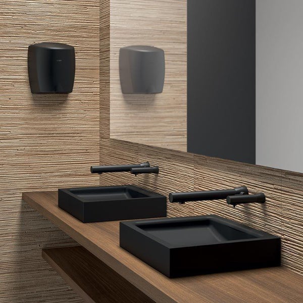 Modernes Badezimmer mit zwei schwarzen Aufsatzwaschbecken, Wandarmaturen und Händetrockner vor einer strukturierten Fliesenwand und Holzwaschtisch.