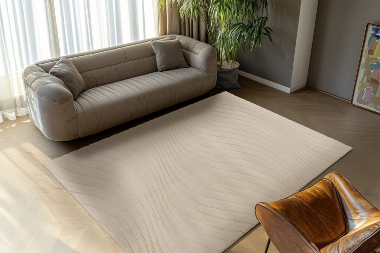 Moderner rechteckiger Teppich mit gewelltem Linienmuster in einem wohnlich eingerichteten Wohnzimmer mit Sofa und Ledersessel.