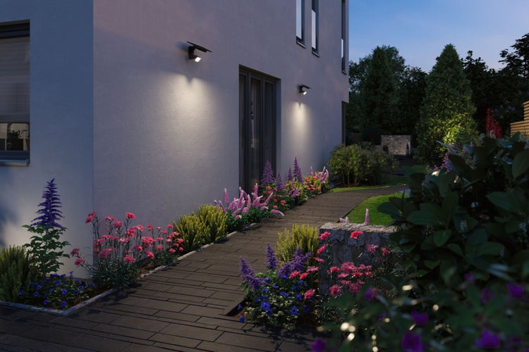 Moderne Hausfassade bei Dämmerung mit zwei Solar-Wandleuchten über einem bepflanzten Blumenbeet und einem Steinweg.
