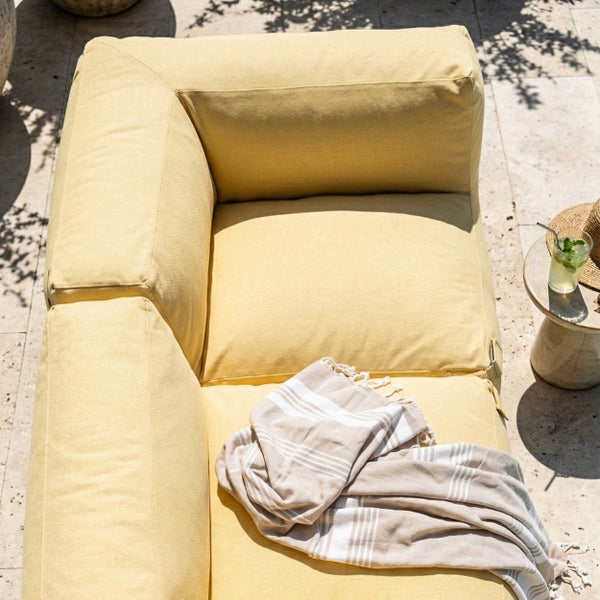 Draufsicht auf ein gelbes Outdoor Loungesofa mit einer gestreiften Decke auf einer Steinterrasse.