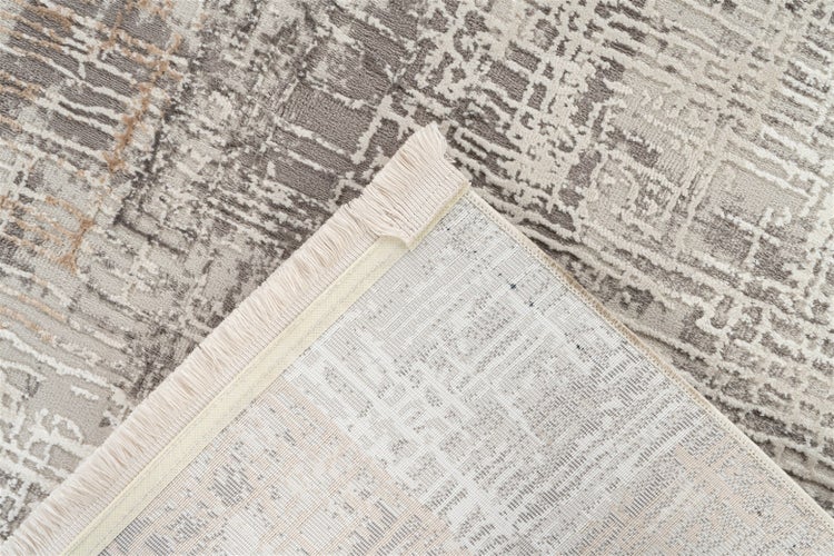 Nahaufnahme eines Teppichs mit abstraktem Muster, eine umgeknickte Ecke zeigt die strukturierte Rückseite und die Fransen.