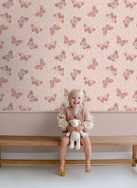 Mädchen sitzt vor einer Wand mit Schmetterlingstapete auf einer Holzbank